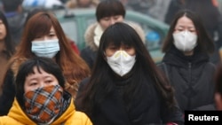 FILE - Commuters wearing masks make their way amid thick haze in the morning in Beijing February 26, 2014. 