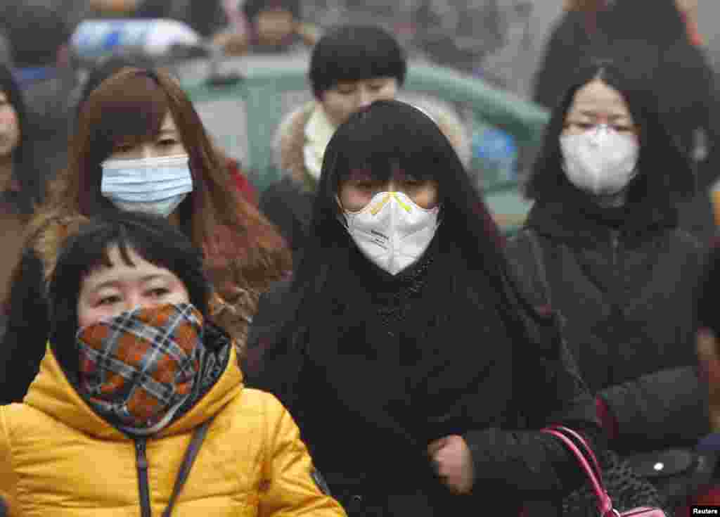 Komuter mengenakan masker berjalan di tengah kabut asap tebal di suatu pagi di Beijing, 26 Februari 2014.