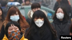 FILE - Commuters wearing masks make their way amid a thick morning haze in Beijing.