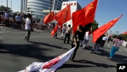 A Chinese woman drags a Japanese flag on the ground as she follows a group holding up Chinese flags during a protest march towards the Japanese Embassy in Beijing, Sept. 18, 2012.