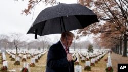El presidente Donald Trump camina bajo la lluvia por la Sección 60 del Cementerio Nacional de Arlington, durante una visita para honrar a veteranos cuando voluntarios colocan coronas en las tumbas por las festividades navideñas.