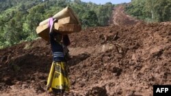FILE: A woman carries a rolled-up mattress at a landslide site in Shisakali village of Bududa district, eastern Uganda, 6.6.2019