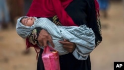 FILE - A Rohingya Muslim woman, who crossed over from Myanmar into Bangladesh, holds her sick daughter and some medicine and walks back toward her shelter in Thaingkhali refugee camp, Bangladesh, Oct. 21, 2017. 