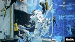 Astronauts practice on a Hubble model underwater at the Neutral Buoyancy Lab in Houston under the watchful eyes of NASA engineers and safety divers.