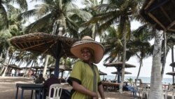 Une vendeuse de chapeaux pose pour une photo sur une plage devant un hôtel à Grand-Bassam, en Côte d'Ivoire, le 28 mars 2021.