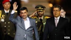 El presidente de Irán saluda a las personas presentes mientras camina junto al vicepresidente venezolano en el aeropuerto Simón Bolívar en Caracas.