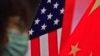 Seorang wanita mengenakan masker duduk di dekat layar yang menunjukkan bendera China dan AS saat dia mendengarkan pidato tentang hubungan kedua negara. 