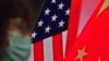 In this Feb. 22, 2021, file photo, a woman wearing a face mask sits near a screen showing China and U.S. flags as she listens to a speech on China-U.S. relations.