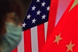 In this Feb. 22, 2021, file photo, a woman wearing a face mask sits near a screen showing China and U.S. flags as she listens to a speech on China-U.S. relations.