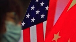 In this Feb. 22, 2021, file photo, a woman wearing a face mask sits near a screen showing China and U.S. flags as she listens to a speech on China-U.S. relations.