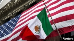 FILE - The flag of Mexico changes in front of a large U.S. flag in front of the New York Stock Exchange Sept. 4, 2015. 