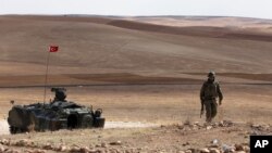 A Turkish soldier stands next to an armored vehicle stationed on a hill top overlooking the fighting positions between Syrian Kurds and Islamic State militants, about 10 kilometers in the west of Kobani in Syria, near Suruc, Turkey, Oct. 2, 2014. 