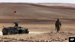 A Turkish soldier stands next to an armored vehicle stationed on a hill top overlooking the fighting positions between Syrian Kurds and Islamic State militants, about 10 kilometers in the west of Kobani in Syria, near Suruc, Turkey, Oct. 2, 2014. 