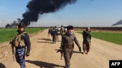 FILE - Members of the Kurdish Peshmerga forces and the Iraqi security forces patrol on a road as smoke billows from the Khubbaz oil field, some 25 km west of the northern city of Kirkuk, Feb. 2, 2015. 
