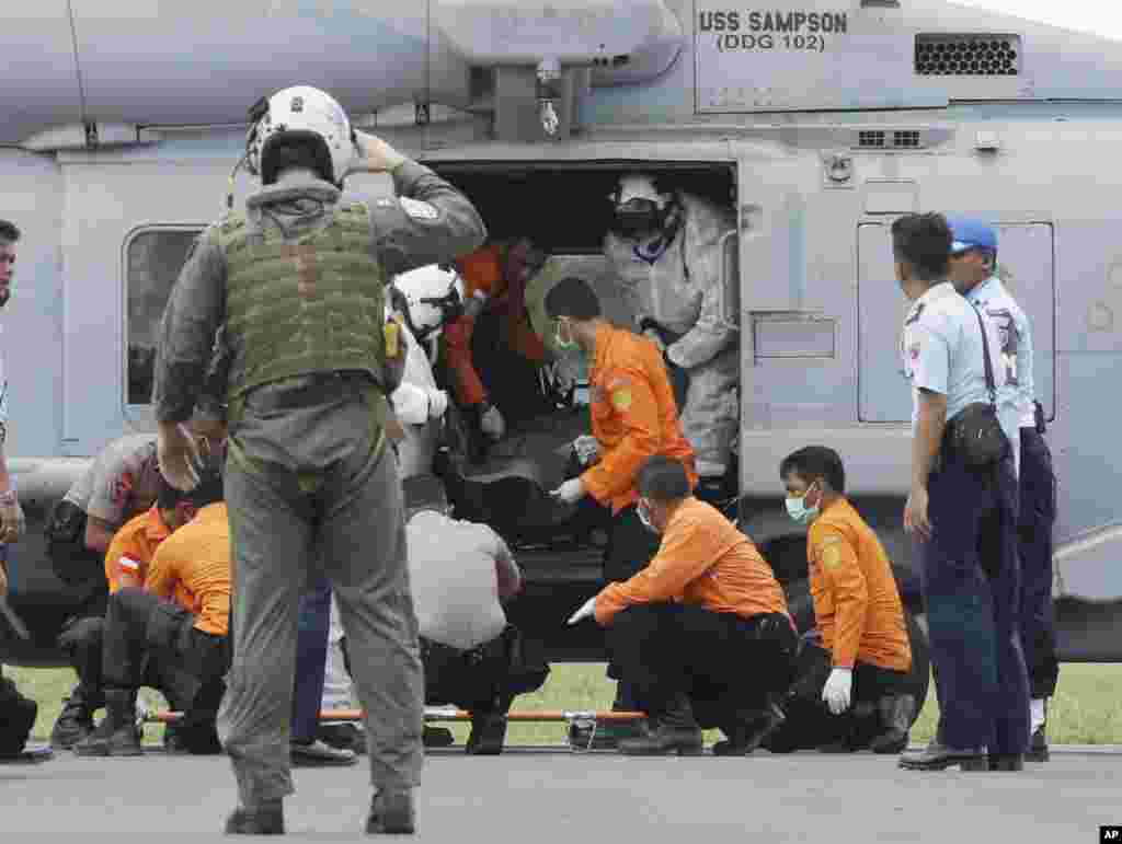 U.S. Navy personnel from USS Sampson unload the body of a victim from AirAsia Flight 8501 from a helicopter as search and rescue personnel and Indonesian policemen receive it in Pangkalan Bun, Indonesia, Friday, Jan. 2, 2015.