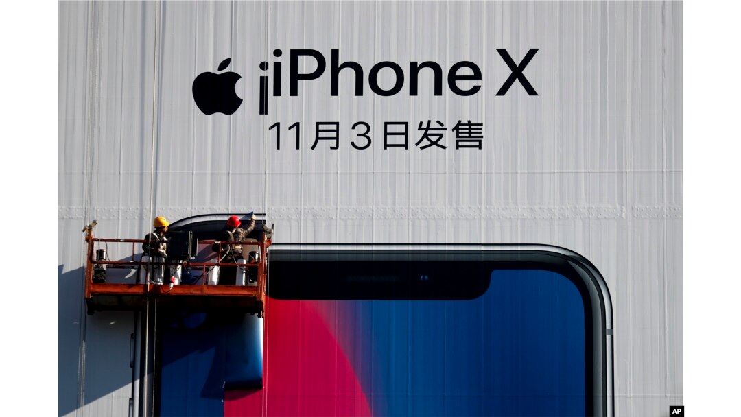 Workers on a suspended platform replace an advertisement poster for the new iPhone X on a building in Beijing, Oct. 30, 2017.