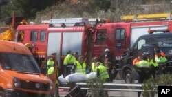 Undertaker workers carry the body of a person killed during a bus accident on the AP7 highway that links Spain with France along the Mediterranean coast near Freginals halfway between Valencia and Barcelona, Sunday, March 20, 2016. 