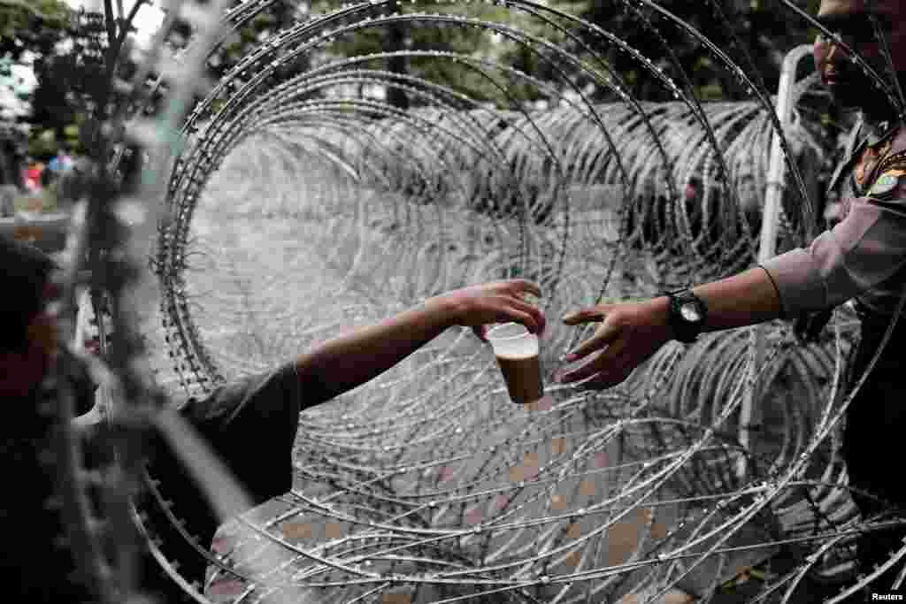 An Indonesian policeman buys a drink as he stands guard near the barbwire outside a court at the blasphemy trial of Jakarta&#39;s incumbent governor Basuki Tjahaja Purnama, also known as Ahok, in Jakarta, Indonesia.