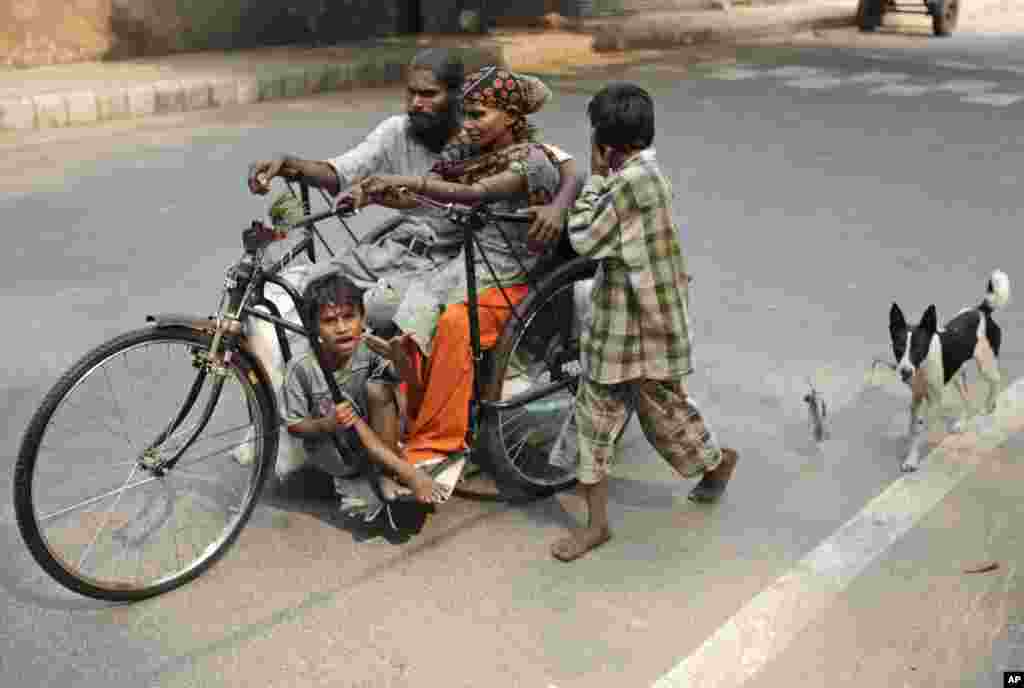 A beggar family commutes on a handcycle with their pet dog following on a leash in New Delhi, India.