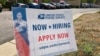 A now hiring sign stands in the parking lot of the University Hills branch of the United States Postal Service, Oct. 12, 2021, in southeast Denver. 