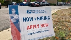A now hiring sign stands in the parking lot of the University Hills branch of the United States Postal Service, Oct. 12, 2021, in southeast Denver. 
