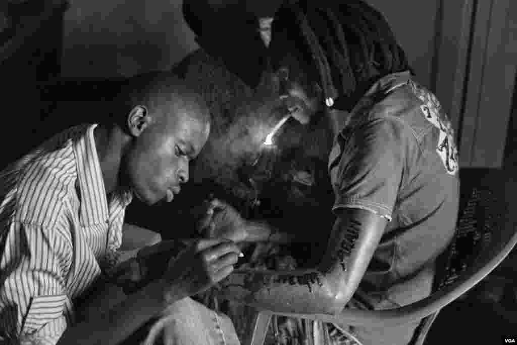 Negnzi Alliy (esquerda), 23 anos, faz uma tatuagem do genocídio do Ruanda com o a frase &quot;never again&quot; (nunca mais) no braço de Tomy. Negnzi Alliy diz &quot;Eu não me preocupo com transmissão do VIH-SIDA através das minhas agulhas. Giporoso está a matar suavemente a nossa geração&quot;. Giporoso, Kigali, Ruanda, Nov. 5, 2013.