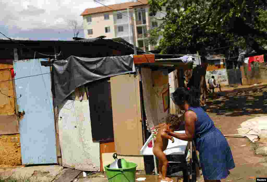 A woman in a slum bathes her child, in front of the new apartments of the &quot;Minha Casa, Minha Vida&quot; (My House, My Life) housing program in Rio de Janeiro, Brazil.