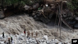 Water gushes down a river as Indian paramilitary soldiers and volunteers stand near a makeshift bridge after it was damaged hampering to evacuate the stranded pilgrims in Govindghat, India, June 22, 2013. 