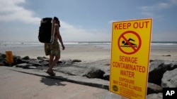FILE - A beachgoer walks past a sign posted to warn people of contaminated water at Torrey Pines State Beach in San Diego, California.