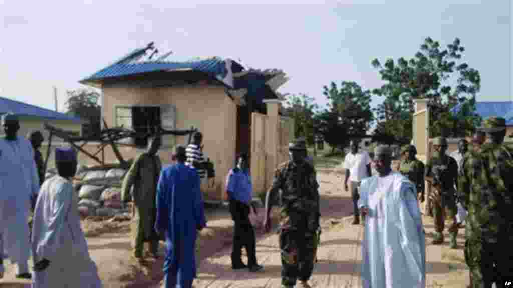 In this photo taken on a mobile phone, on Thursday, Sept . 19, 2013, government officials stand by a damaged house following an attack by Boko Haram, in Benisheik, Nigeria.