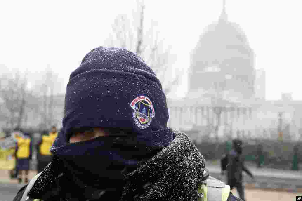Snow begins to stick on the cap and jacket of a U.S. Capitol Police, in front of the U.S. Capitol in Washington D. C., Jan. 22, 2016. 