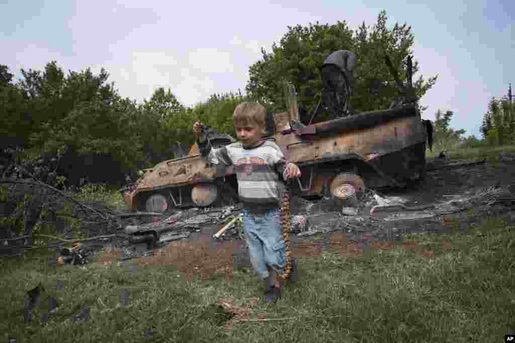 A boy plays with a machine gun belt as local citizens collect parts of a destroyed amored personnel carrier, village of Oktyabrskoye village, near Kramatorsk, eastern Ukraine, May 14, 2014.