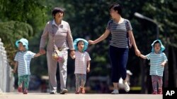 In this photo from June 1, 2017, women walk with children wearing matching hats as they cross a bridge in a public park on International Children's Day in Beijing.