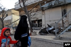 A Syrian woman and child walk past the shuttered doors of a restaurant which was the site of a suicide attack targeting US-led coalition forces in the northern Syrian city of Manbij which killed four US servicemen the previous day on Jan. 17, 2019.