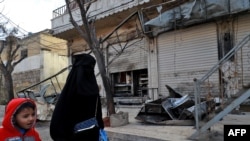 A Syrian woman and child walk past the shuttered doors of a restaurant which was the site of a suicide attack targeting US-led coalition forces in the northern Syrian city of Manbij which killed four US servicemen the previous day on Jan. 17, 2019.