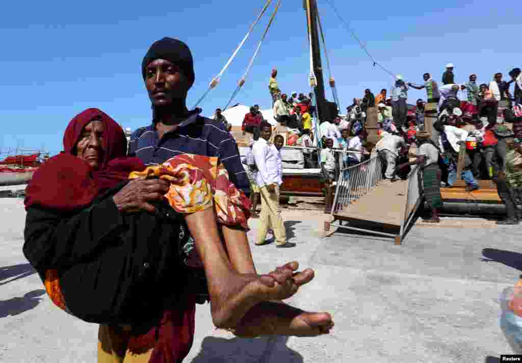 Seorang pria menggendong seorang perempuan tua dari kapal yang membawa orang-orang yang melarikan diri dari Yaman, di pelabuhan Bosasso di kawasan Puntland.