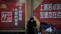 A migrant worker sits next to his belonging against a wall displaying a Chinese government propaganda message at the Beijing railway station in Beijing, Monday, Jan. 21, 2019.