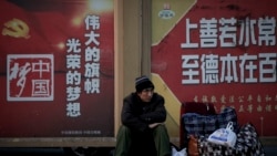 A migrant worker sits next to his belonging against a wall displaying a Chinese government propaganda message at the Beijing railway station in Beijing, Monday, Jan. 21, 2019.