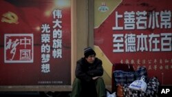 A migrant worker sits next to his belonging against a wall displaying a Chinese government propaganda message at the Beijing railway station in Beijing, Monday, Jan. 21, 2019.