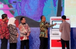 Seorang warga mencoba mesin Anjungan Dukcapil Mandiri untuk mencetak Kartu Keluarga (Foto:VOA/ Petrus Riski).