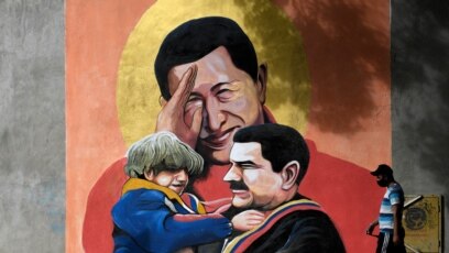 Một người đi ngang qua tranh tường vẽ cố TT Hugo Chavez, giữa, giơ tay chào TT Nicolas Maduro, phải, đang bồng một đừa trẻ ở Caracas. (Photo by Federico PARRA / AFP)