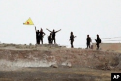 Fighters with the Kurdish People's Protection Units, or YPG, wave their yellow triangular flag on the outskirts of Tal Abyad, Syria, June 15, 2015.