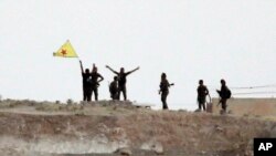 Fighters with the Kurdish People's Protection Units, or YPG, wave their yellow triangular flag on the outskirts of Tal Abyad, Syria, June 15, 2015.