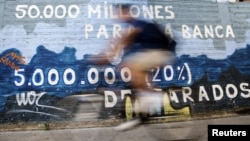 A man rides his bicycle past graffiti that says '50,000 million for rescuing banks and five million unemployed' in Burgos, central Spain, June 28, 2012. 