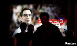 People pass a campaign poster for Social Democratic Union presidential candidate Stevo Pendarovski in Skopje, North Macedonia, May 2, 2019.