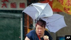 Taiwan Typhoon: A woman eats and struggles with her umbrella against powerful gusts of wind generated by typhoon Megi across the the island in Taipei, Taiwan, Tuesday, Sept. 27, 2016. 