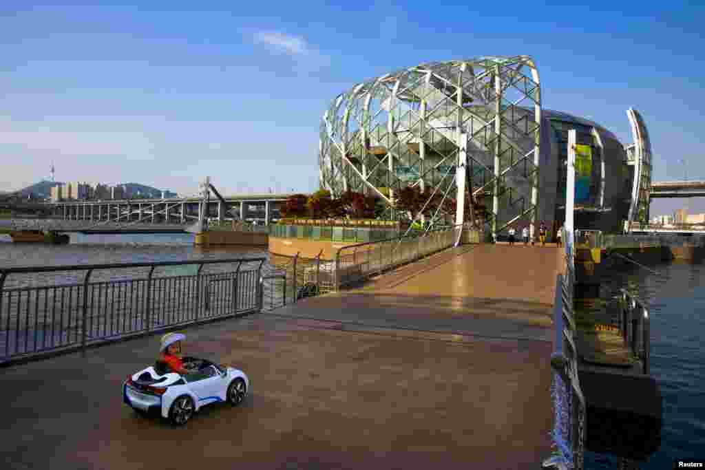 A child drives an electric toy car on a walkway connecting sections of the Floating Island, or Some Sevit in Seoul, South Korea.