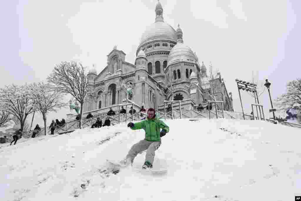 Geoffrey, 32, rides his snowboard down the Montmartre hill, with the Sacre Coeur Basilica in background in Paris, France.