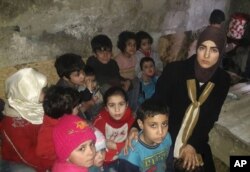 This March 11, 2018 photo, provided by Deana Lynn, from Detroit, Michigan, shows her, with her kids and other Syrian children at a shelter where they hide from Russian and Syrian government forces airstrikes, in eastern Ghouta, a suburb of the Syrian capital Damascus.
