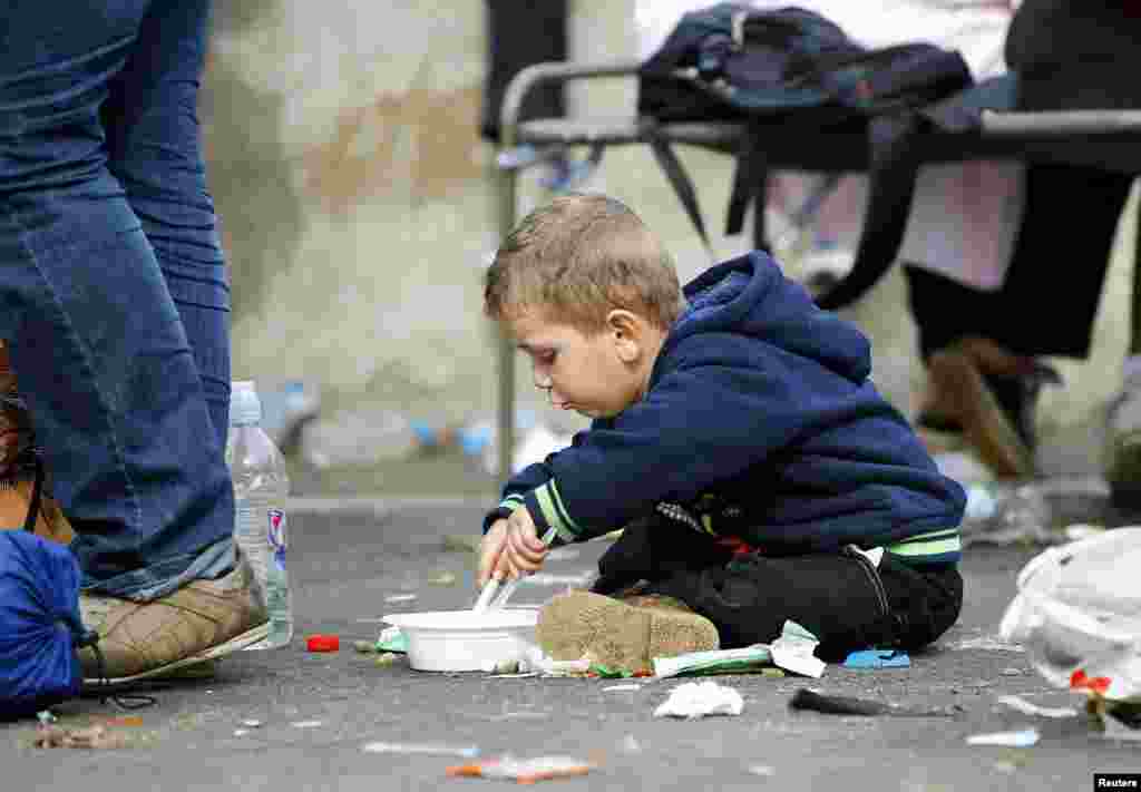 A migrant boy eats on the ground at the check point Heiligenkreuz, Austria, Sept. 20, 2015, located at the border with Hungary. Hungary and Croatia traded threats as thousands of exhausted migrants poured over their borders, deepening the disarray in Europe over how to handle the tide of humanity.